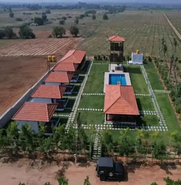 The managed farmland from the air: a row of tile-roofed cottages along a lawn, a pool and a timber watchtower, with planted fields running to the horizon.